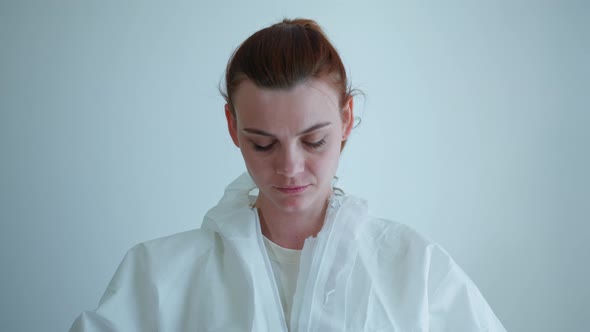 Tired Doctor Woman Putting on Medical Suit for Protection Against Coronavirus for Examining Sick