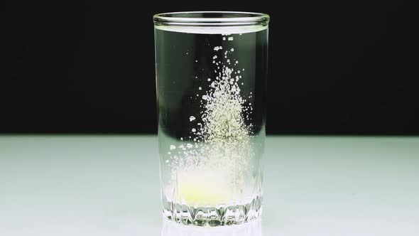 An Effervescent Tablet Against Pain Falls Into a Glass and Dissolves Close-up Slow-motion Shot of