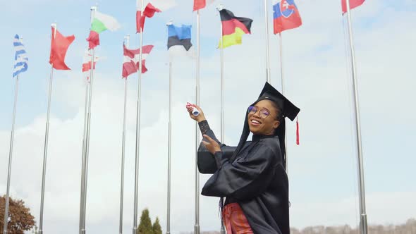 A Young AfricanAmerican Woman Rejoices and Points with a Diploma to the Flags of Different Countries