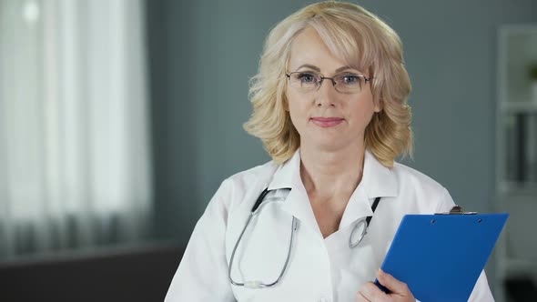 Mature Doctor Looking Into Camera Guaranteeing High Quality of Medical Services