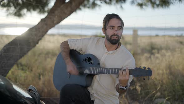 Bearded Man Playing Guitar Outdoors Near Car and Singing Rhythmic Agile Song Roadside