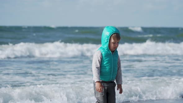 Toddler Boy in Waistcoat Is Playing with Sand on Sea Side.