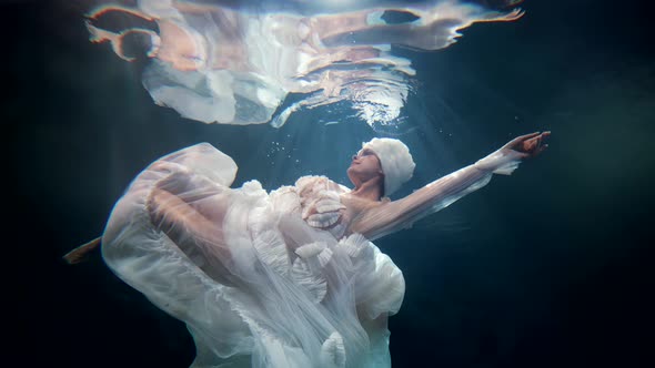 Enigmatic Lady in White Gorgeous Dress is Swimming in Mysterious Depth of Magical Sea or Ocean