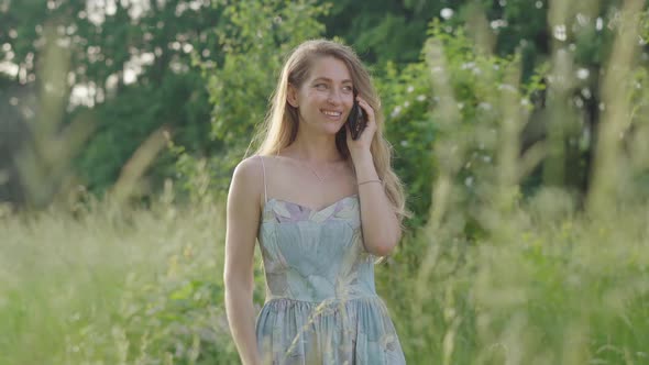 Laughing Beautiful Girl Talking on the Phone on Sunny Meadow. Portrait of Young Brunette Caucasian