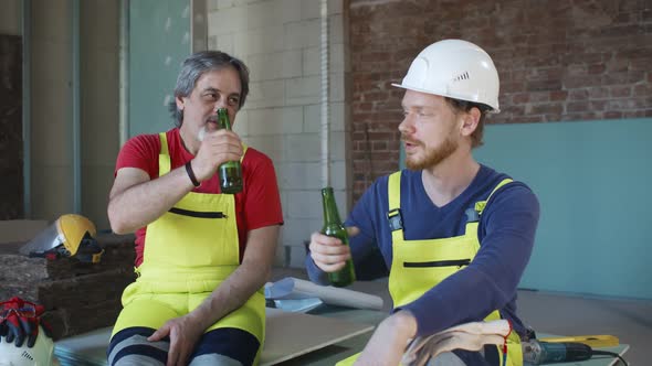 Construction Workers in Work Wear, Helmets Drink Beer From Bottle at Work