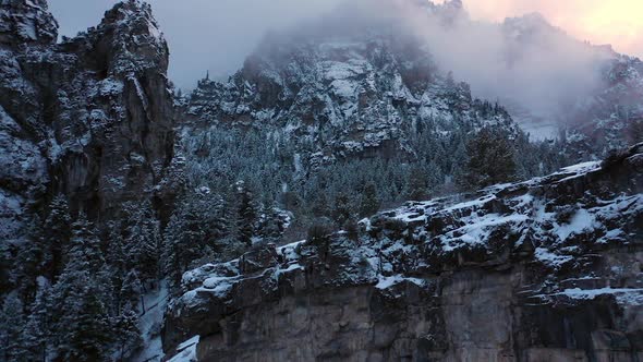 Panning aerial view of jagged cliffs in winter forest landscape