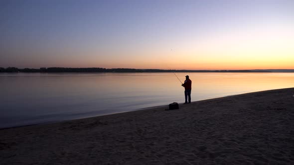A Man Is Fishing at Sunrise By the River. The Yellow Sun Rises From the Horizon. Silhouette of a