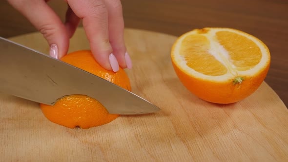 Closeup of a Woman Slicing an Orange with a Knife on a Chopping Board