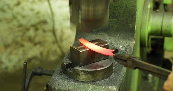 Bladesmith working with hot blade at hydraulic press