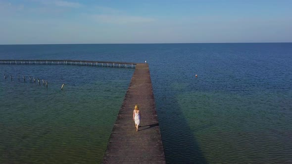 A Girl Walks on a Wooden Pier Near the Sea