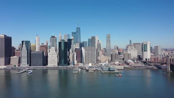 An aerial view over the east East River on a sunny day with blue skies. The drone camera, facing low