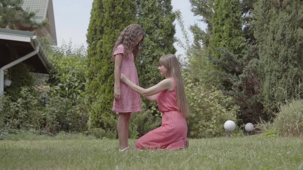 Young Beautiful Woman with Long Hair Sitting on the Grass with Her Daughter in the Garden. Family