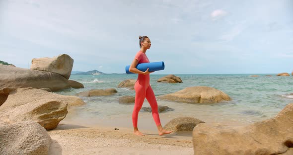 Woman Walking on the Beach for Morning Exercise She Carry Blue Yoga Mat and Wears Pink Sports Suit