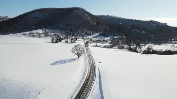 Slow aerial view over snow covered valley with single bare tree stating stoically in the field.