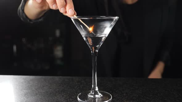 Female Bartender Setting Fire with Burning Stick on Alcohol Cocktail in Slow Motion. Fire Ignition