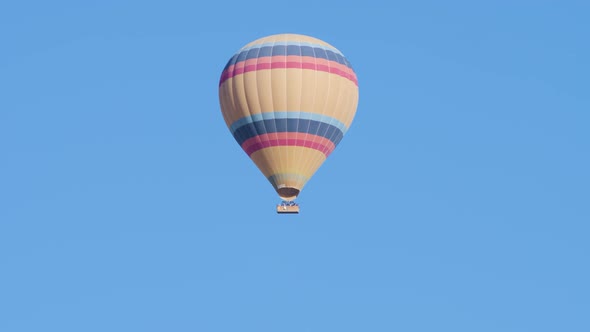 Hot Air Balloon Striped with a Basket of Tourists Flying High in the Sky