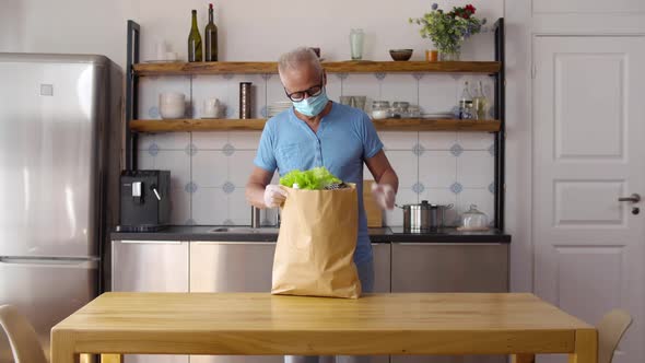 Aged Man in Protective Mask Unpack Bag with Groceries in Kitchen