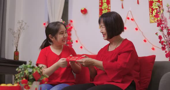 Happy Senior Asian Woman Giving Her Granddaughter A Lucky Red Envelope for Chinese New Year Gift.