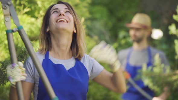 Portrait of Cute Caucasian Woman Showing Thumb Up Holding Big Garden Cutter in the Foreground