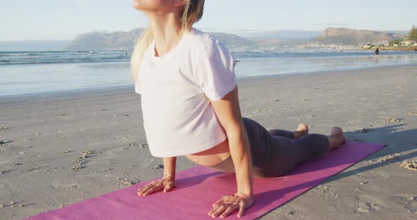 Caucasian woman practicing yoga, stretching at the beach