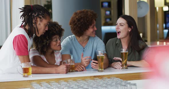 Diverse group of happy friends drinking beers and using smartphone at a bar