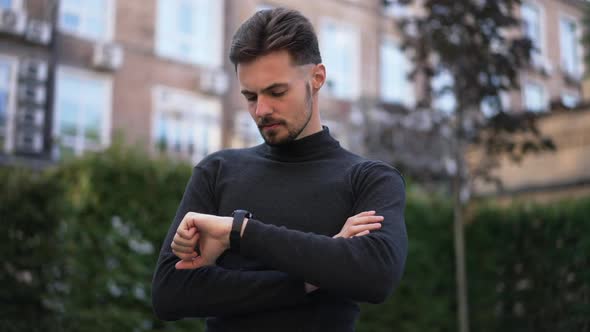 Portrait of Serious Caucasian Young Businessman Checking Time on Wristwatch Looking Around Standing