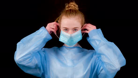 Serious Woman Doctor in a Blue Medical Coat Put on a Medical Mask Looking at Camera