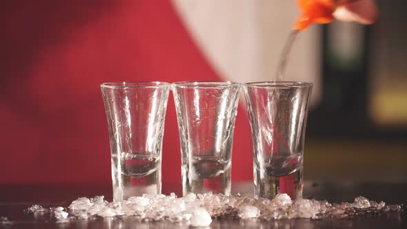 Barman Hand Pours Vodka in Short Transparent Glasses with Ice Chips for Cooling