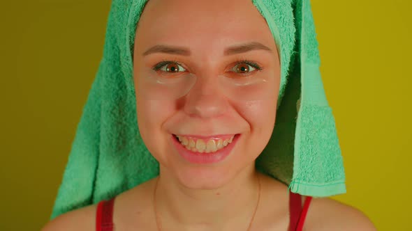 Woman with Towel on Head and Patches Under Her Eyes Smiles Looking at Camera