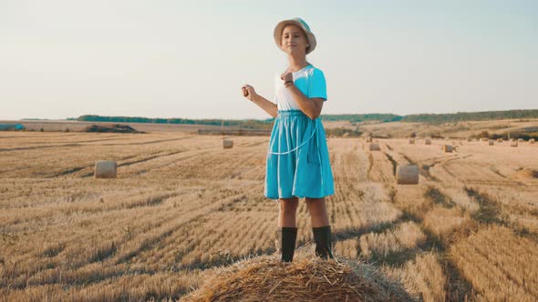 Little Girl in a Field with Hay Jump at Sunset. Girl Near a Hay Bale in the Countryside.