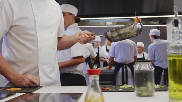 Professional Caucasian male chef in a restaurant kitchen preparing food using a frying pan