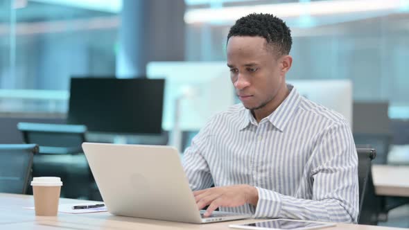 Attractive African Businessman Looking at Camera While Using Laptop in Office