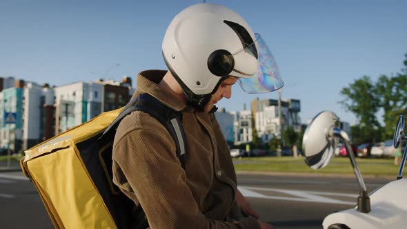 A Delivery Man in a Helmet on a Scooter Who Checks the Delivery Address on the Phone