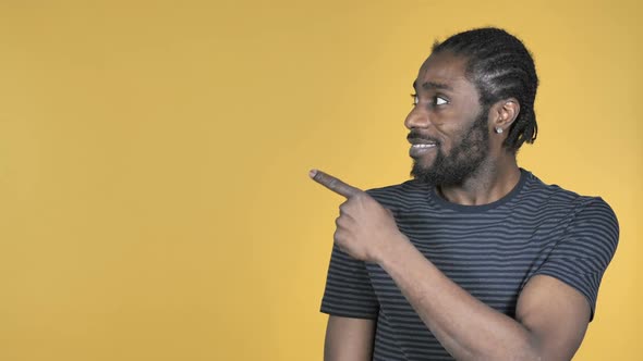 Casual African Man Pointing with Finger on Side Yellow Background