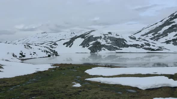 Aerial Top notch Drone Fly above the clearing of frozen lake Isoba, rocky and snowy trekking route,