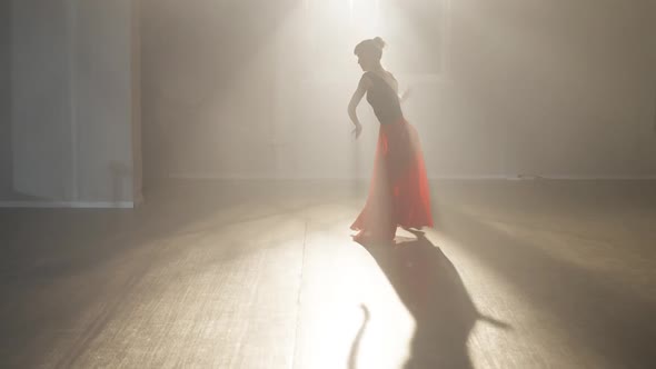 Wide Shot of Slim Professional Ballerina Rehearsing Dance in Backlit Fog Indoors