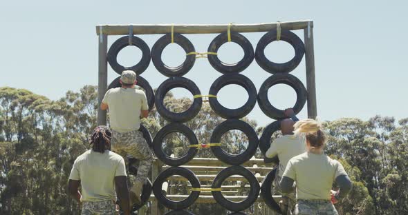 Diverse group of soldiers climbing tyre wall on army obstacle course in the sun