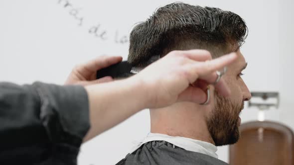 Barber Cutting Hair with Scissors to a Handsome Young Man