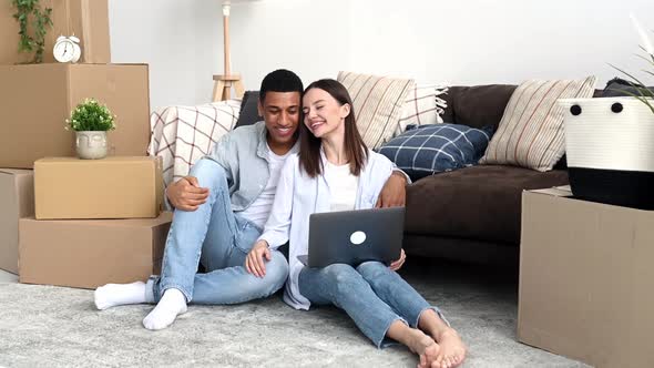 Happy Joyful Multiracial Married Couple in Love Bought New Housing Sit Among Boxes with Things for