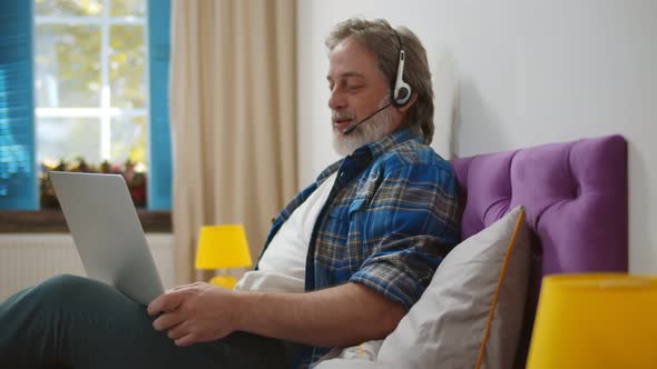 Modern Senior Man Talk on Video Call on Laptop Lying in Bed at Home