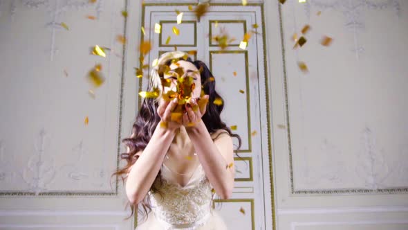 Young Brunette Woman with Red Lips Blows Gold Confetti