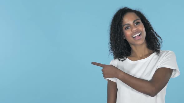 African Girl Pointing with Finger on Side Blue Background