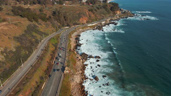 Aerial view following Avenida Borgoño waterfront traffic tilting up to Reñaca sunny cityscape coastl