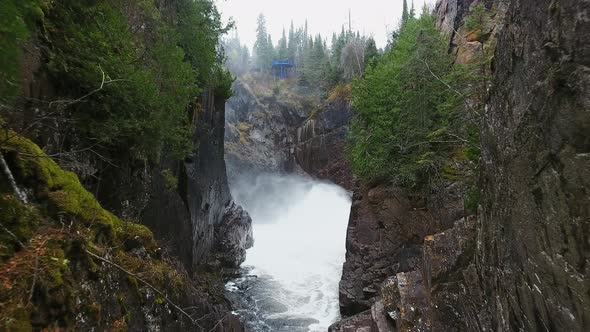 Drone camera approaches stormy waterfall in wooded hills in Aguasabon Falls, Ontario, Canada