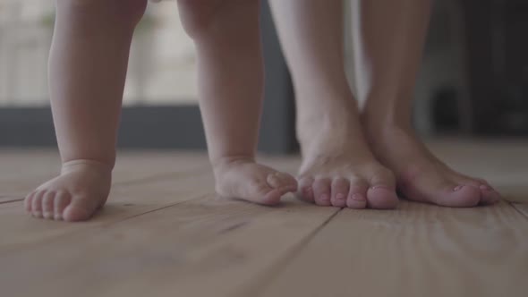 Feet of a Young Woman and Her Baby Standing on the Floor at Home Close-up. Concept of a Happy Family