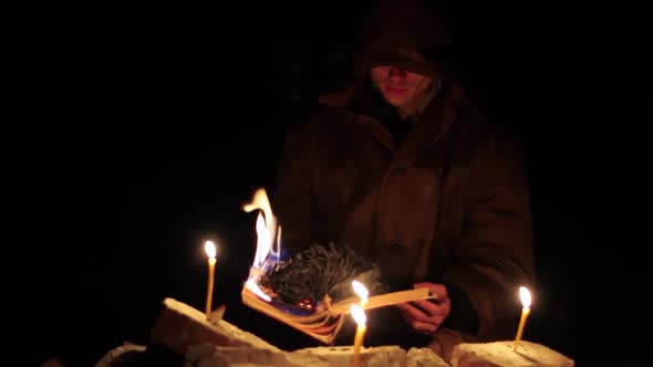 a Man in a Cloak with a Hood is Reading a Hot Book with Candles on the Floor