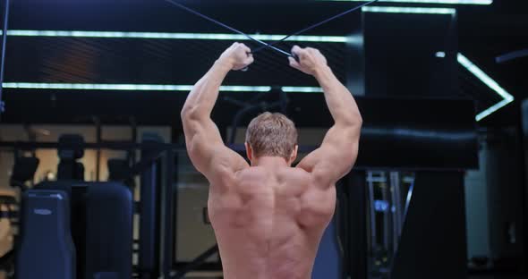 Athlete a Bodybuilder Stretches the Harnesses Behind the Head on the Simulator Trains the Latissimus