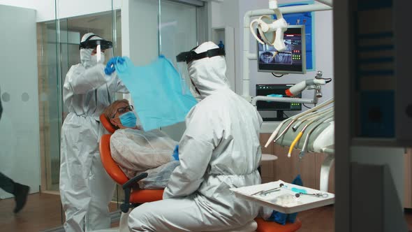 Nurse in Coverall Putting Dental Bib To Woman During Examining