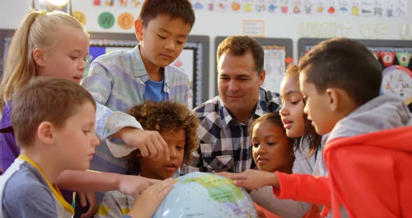 Front view of Caucasian male teacher teaching the kids about the globe in the classroom 4k