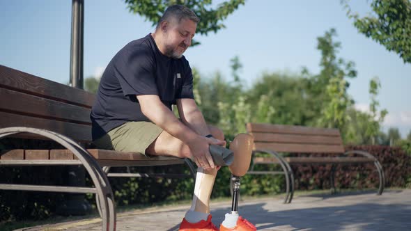 Mature Caucasian Amputee Putting on Prosthesis in Slow Motion Sitting on Bench Talking